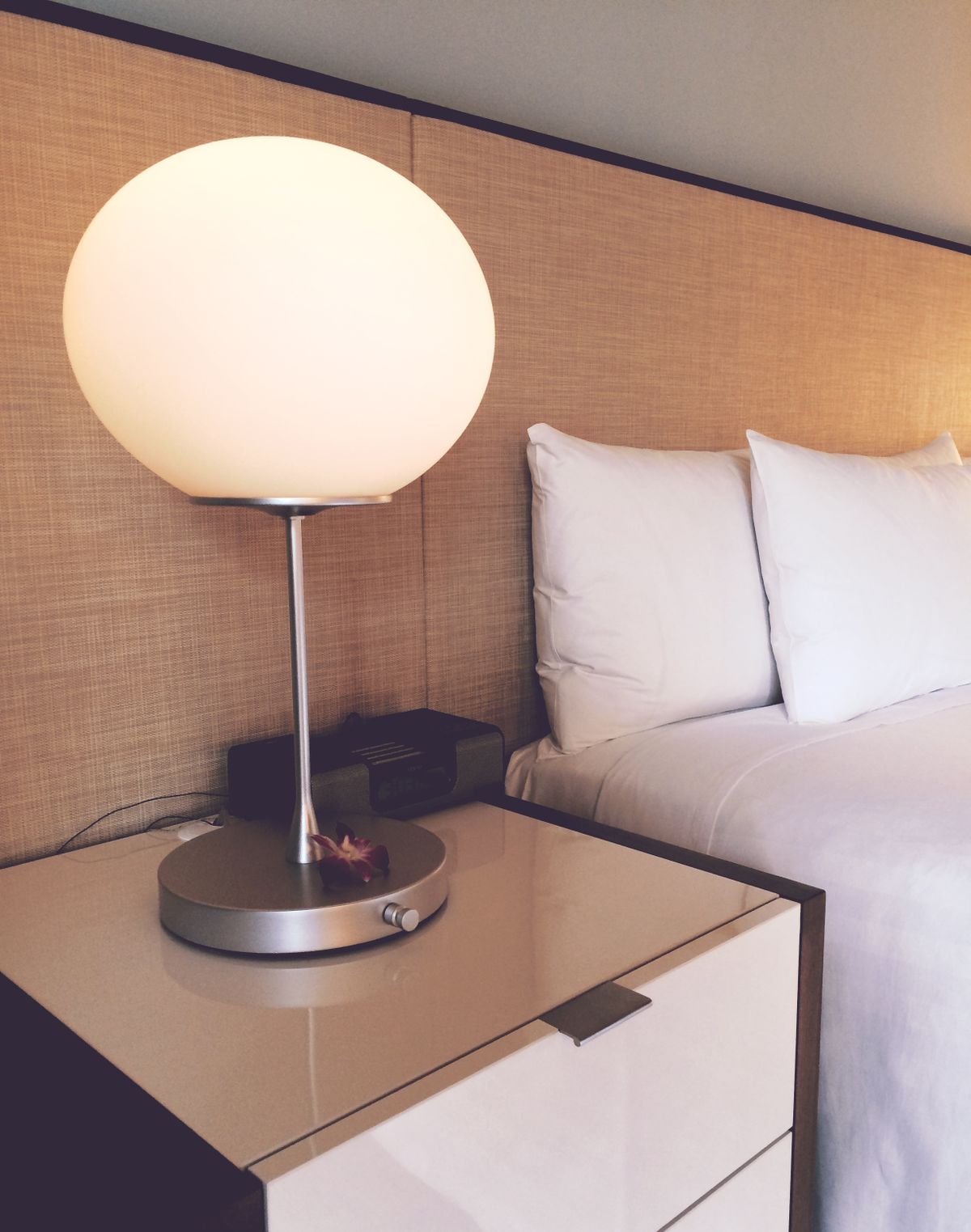 A bedside table with a globe lamp and a made bed with white pillows